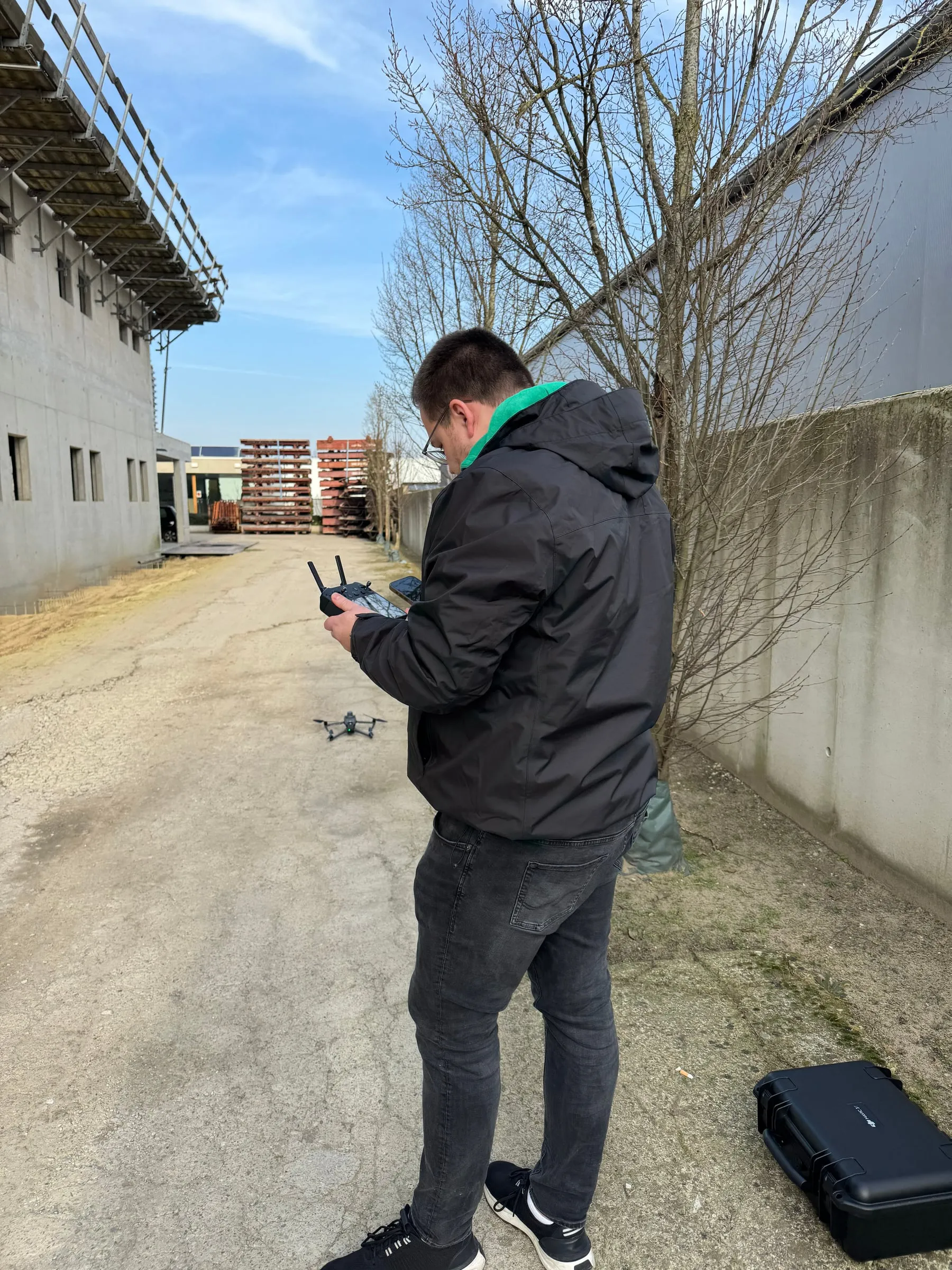 André Meschkat mit Fernsteuerung vor einer Halle im Rohbau, die Drohne schwebt vor ihm über dem Boden